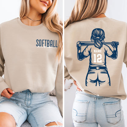 A woman wearing a beige sweatshirt with a graphic of a female softball player on the back, and the word "SOFTBALL" printed on the front.